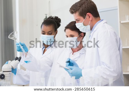 Scientists looking at beaker and taking notes in laboratory