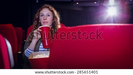 Young woman watching a film and drinking a soda at the cinema
