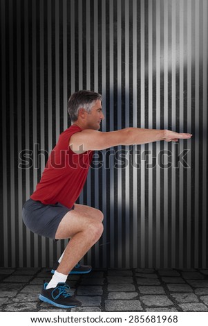 Fit man doing a squat against dark grey room