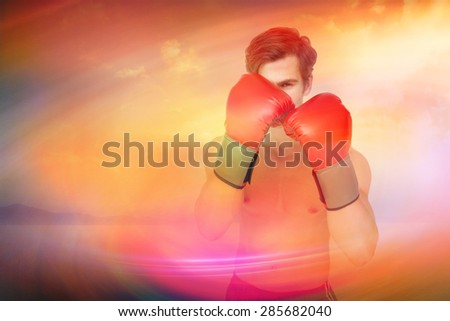 Muscly man wearing red boxing gloves in guard position against desert landscape