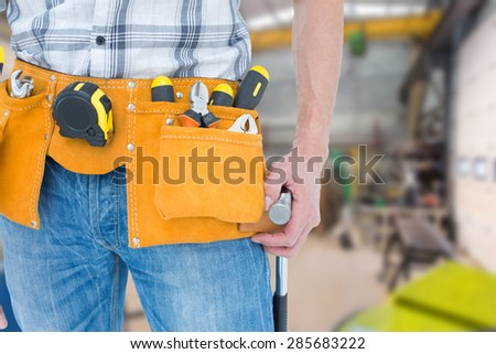 Technician with tool belt around waist against workshop