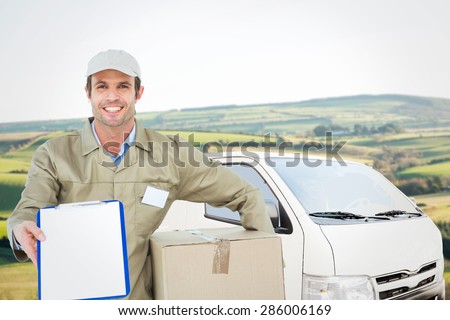 Happy delivery man with box showing clipboard against scenic landscape