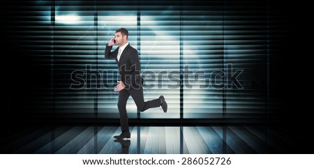Businessman running on the phone against room with large window looking on city