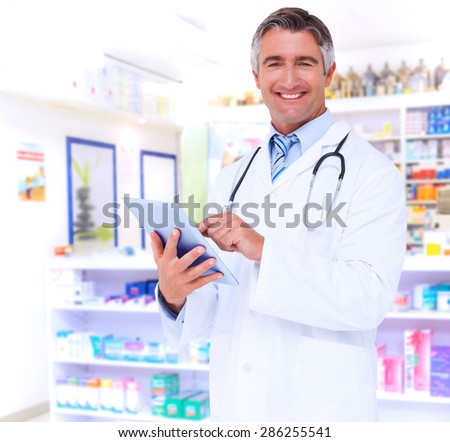 Happy doctor using tablet pc against close up of shelves of drugs