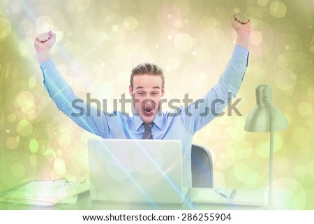 Cheering businessman at laptop against yellow abstract light spot design