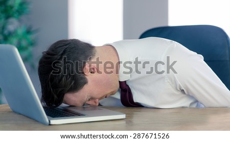 Exhausted businessman sleeping head on laptop in his office