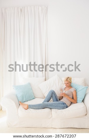 appy blonde woman using her mobile on the sofa at home in the living room