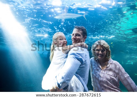 Happy family looking at camera behind a fish tank at the aquarium