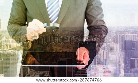 Businessman looking at tablet with magnifying glass against new york
