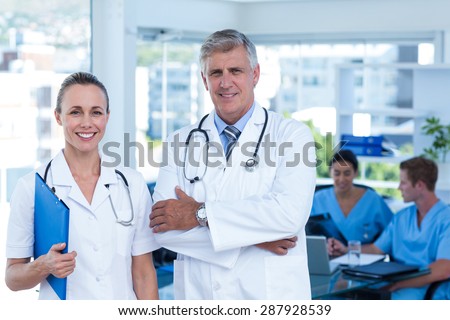 Team of doctors standing arms crossed and smiling at camera in medical office