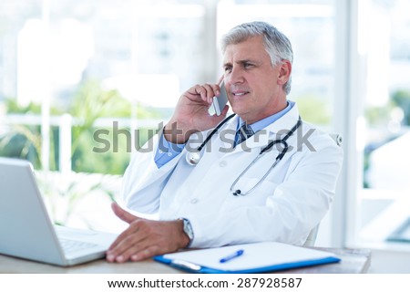 Smiling doctor having phone call at his desk in medical office