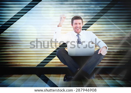 Businessman using laptop and cheering against window overlooking city