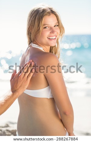 Handsome man putting sun tan lotion on his girlfriend at the beach