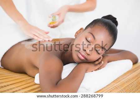 Masseuse pouring massage oil on a pretty woman back at the health spa
