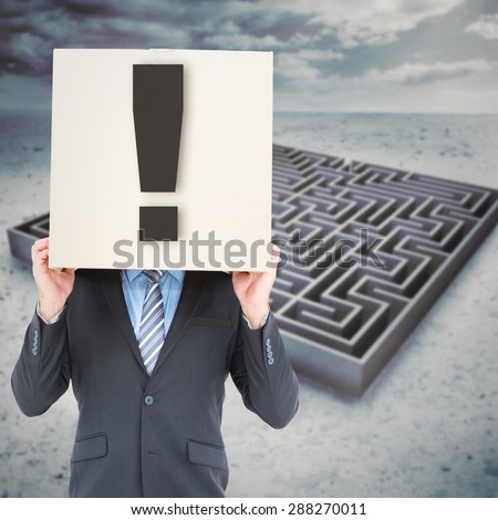 Businessman hiding head with a box against big maze under cloudy sky