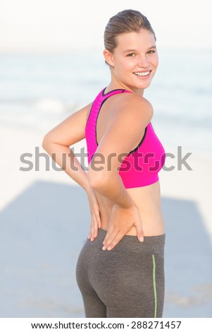 Portrait of beautiful fit woman looking at camera with hands on back at the beach