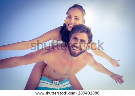 Handsome man giving piggy back to his girlfriend at the beach