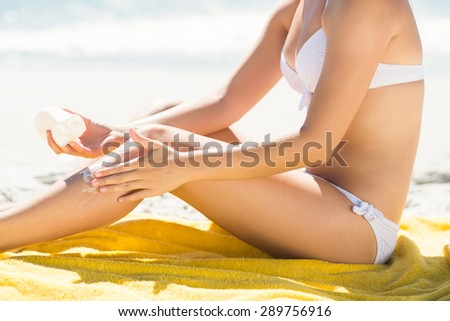 Close up view of Pretty blonde woman putting sun tan lotion on her leg at the beach