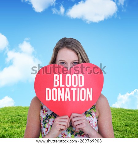 Woman holding heart card against sky and field