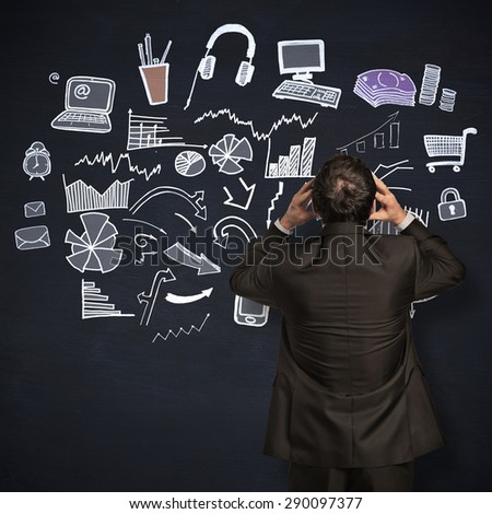 Stressed businessman with hands on head against blackboard