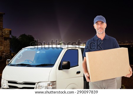 Happy delivery man holding cardboard box against cityscape by night