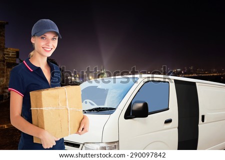 Happy delivery woman holding cardboard box against cityscape by night