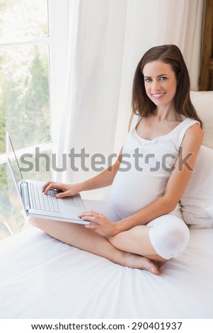 Smiling pregnancy sitting on bed at home in bedroom