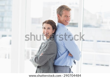 Smiling businesswoman back-to-back with colleague in an office