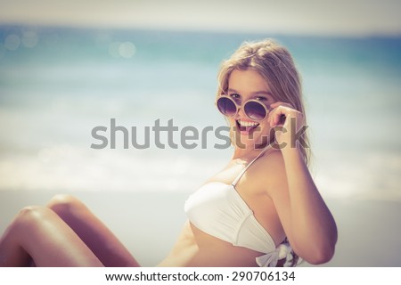 Smiling pretty blonde wearing sun glasses and looking at camera at the beach