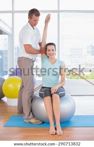 Woman stretching her arm with trainer in fitness studio