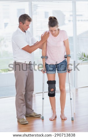 Doctor helping his patient walking with crutch in medical office