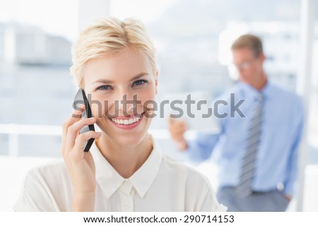 Businesswoman having a phone call with colleague in background in an office