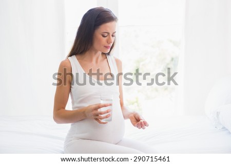Pregnancy sitting on the bed taking a vitamin at home in bedroom