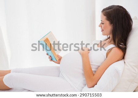 Smiling pregnancy reading in his bed at home in bedroom