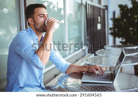 Young businessman drinking coffee beside a laptop outside a cafe