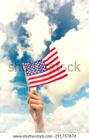 Hand waving american flag against blue sky with white clouds