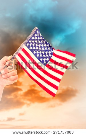 Hand waving american flag against green grass under blue and orange sky