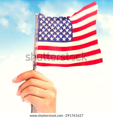 Hand waving american flag against field of grass under blue sky