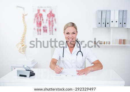 Smiling doctor writing on clipboard at her desk in medical office