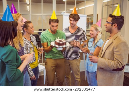 Businessman blowing candles on her birthday cake in the office