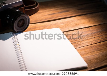 Open notepad next to the camera on wooden table