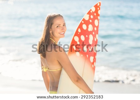 Pretty brunette holding surf board at the beach