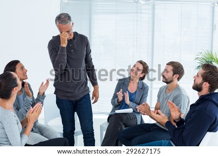 Rehab group applauding delighted man standing up at therapy session