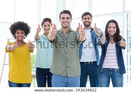 Young creative business people gesturing thumbs up at office