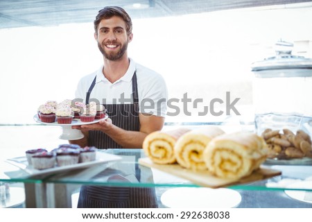 Smiling worker holding cupcakes behind the counter at bakery