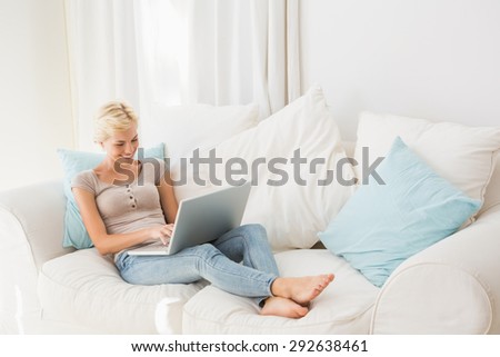Smiling blonde woman using her laptop in the sofa at home in the living room