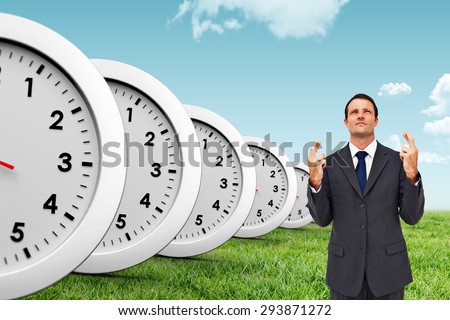 Serious businessman with fingers crossed is looking up against blue sky over green field