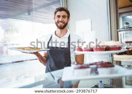 Smiling worker holding pastry behind the counter at bakery