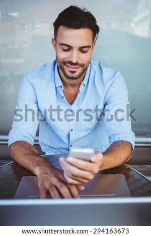 Smiling businessman using phone while working on laptop outside the cafe