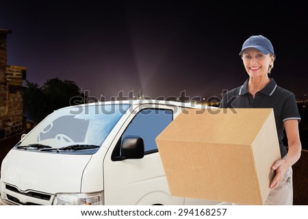 Happy delivery woman holding cardboard box against cityscape by night